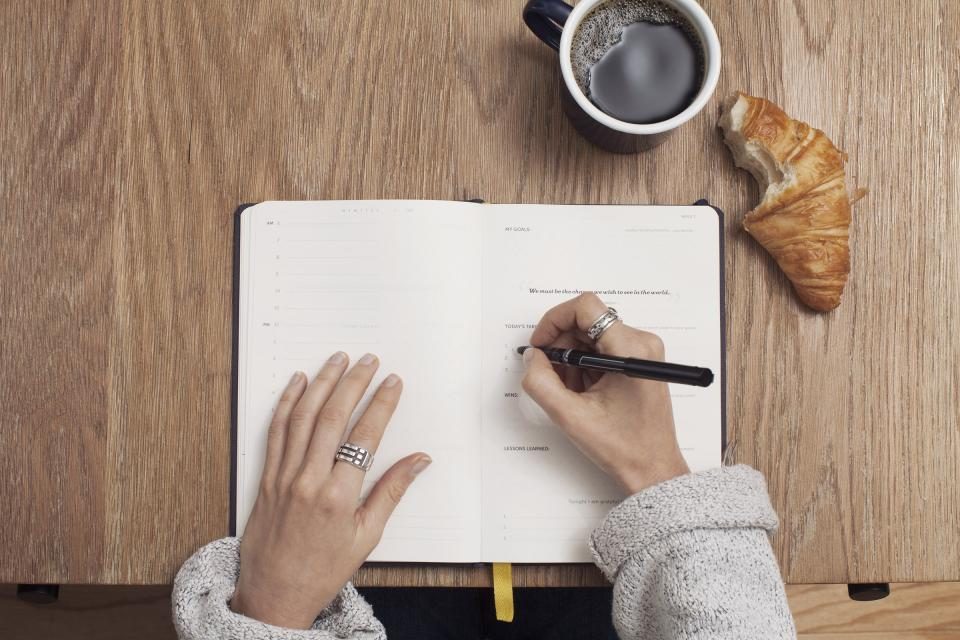 Hands writing in an open journal beside a cup of coffee